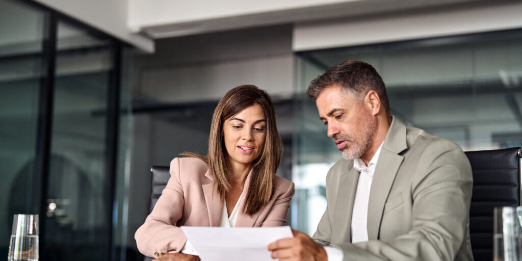 Two professional executives discussing financial accounting papers working together in office. Mature business woman manager consulting older man client holding legal documents at meeting.